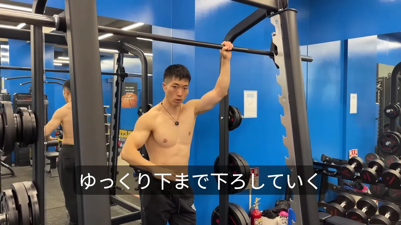 バーを握り『ゆっくり下まで下ろしていく』動作を示すジムの場面