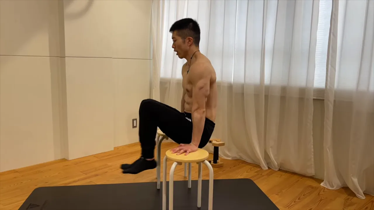 椅子を押して両脚を前へ伸ばしたLシットキックアウトの姿勢
