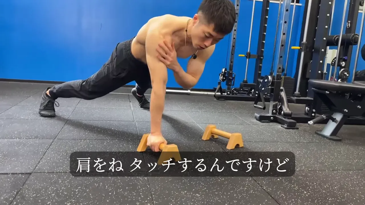 足を広げたプランク姿勢で片手を肩に当てる動作をしている
