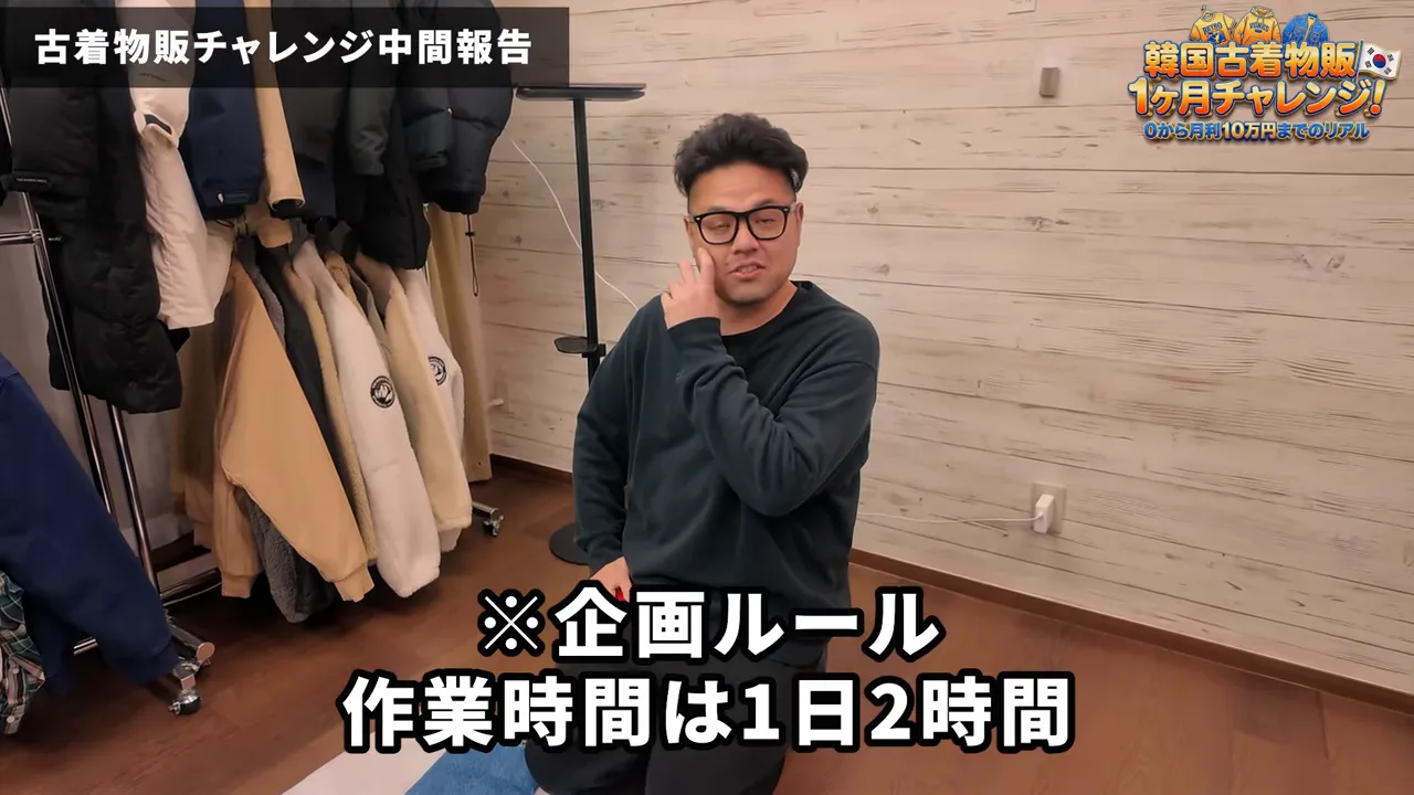 撮影スペースで膝をつく人物とハンガーラック、画面下に「作業時間は1日2時間」の字幕