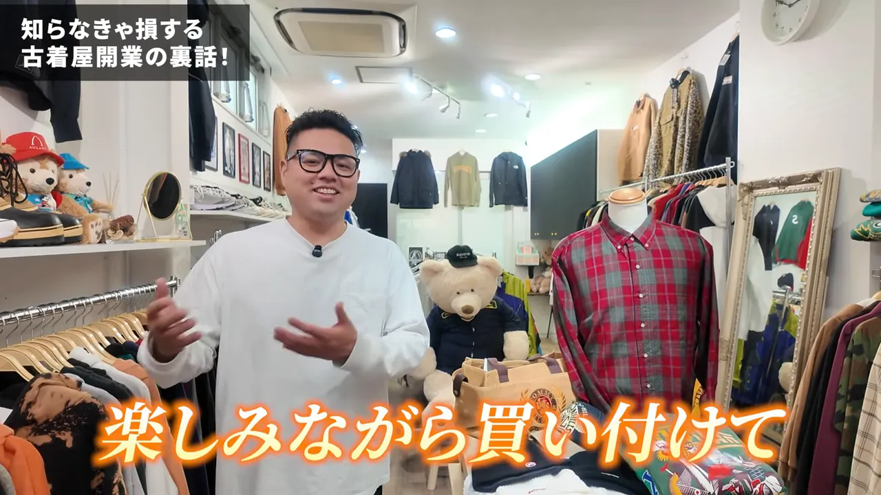 手を動かしながら説明する店主、左右に洋服のラックとマネキンが並ぶ古着屋の明るい店内写真。