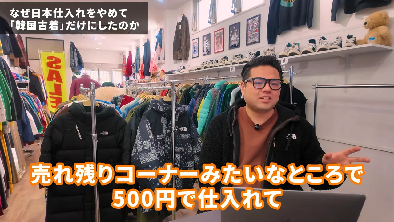 国内仕入れで利益が残りにくい状況を説明する男性と古着ラック