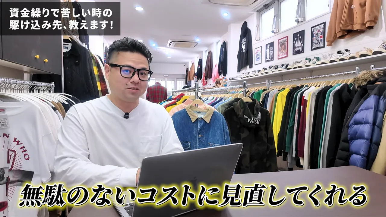 店舗の中でラップトップを前に話す人物と洋服ラック、下部に『無駄のないコストに見直してくれる』というテロップ