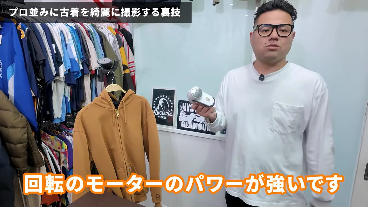 パーカーの横で回転式毛玉取り器を手に持ち見せているワイドショット