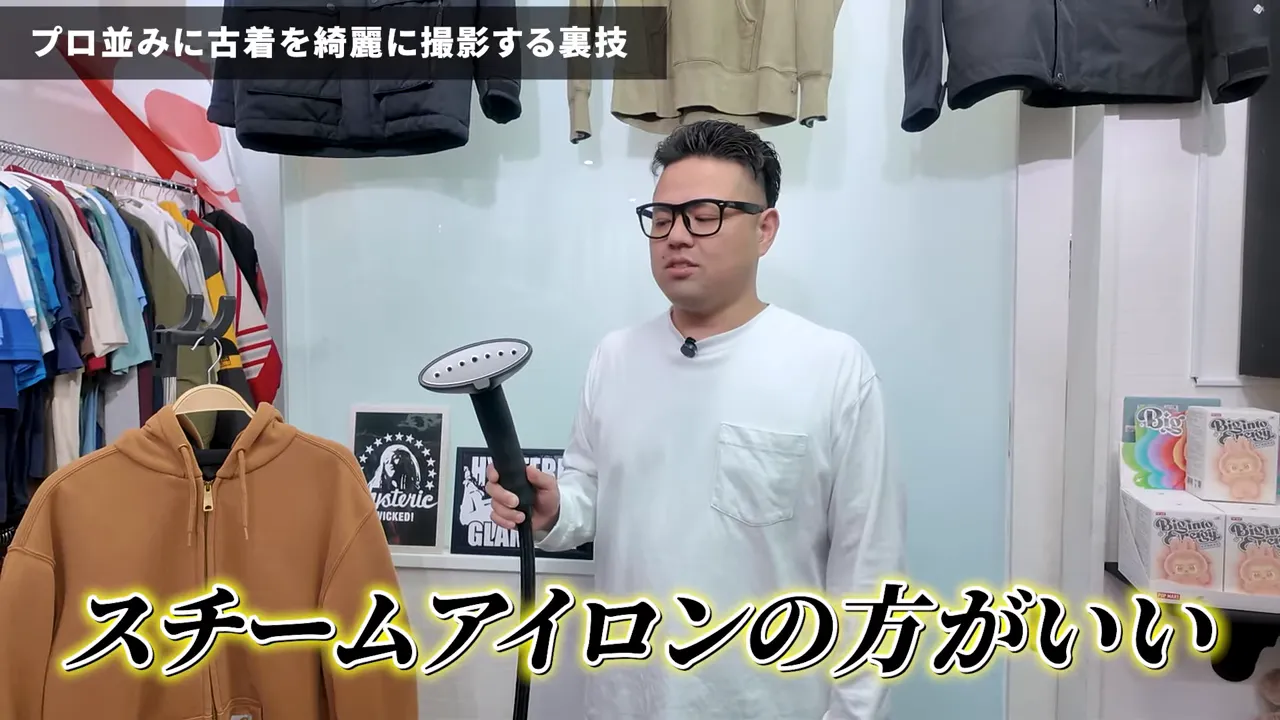 スチームアイロンのヘッドを手に持ち、ハンガーにかけたパーカーのそばで説明しているクローズショット