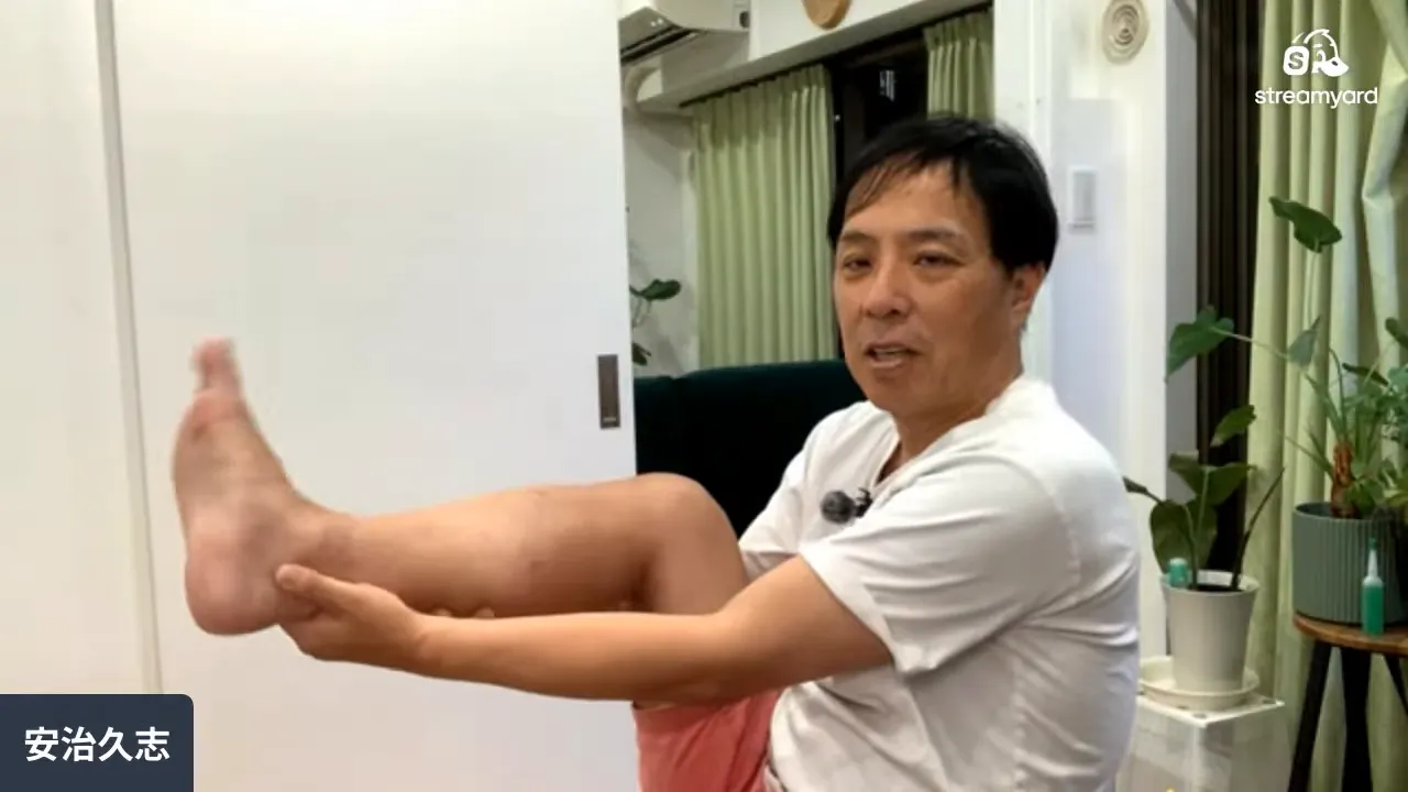 床に座った男性が両足を前に出して足首周辺を手で押さえている