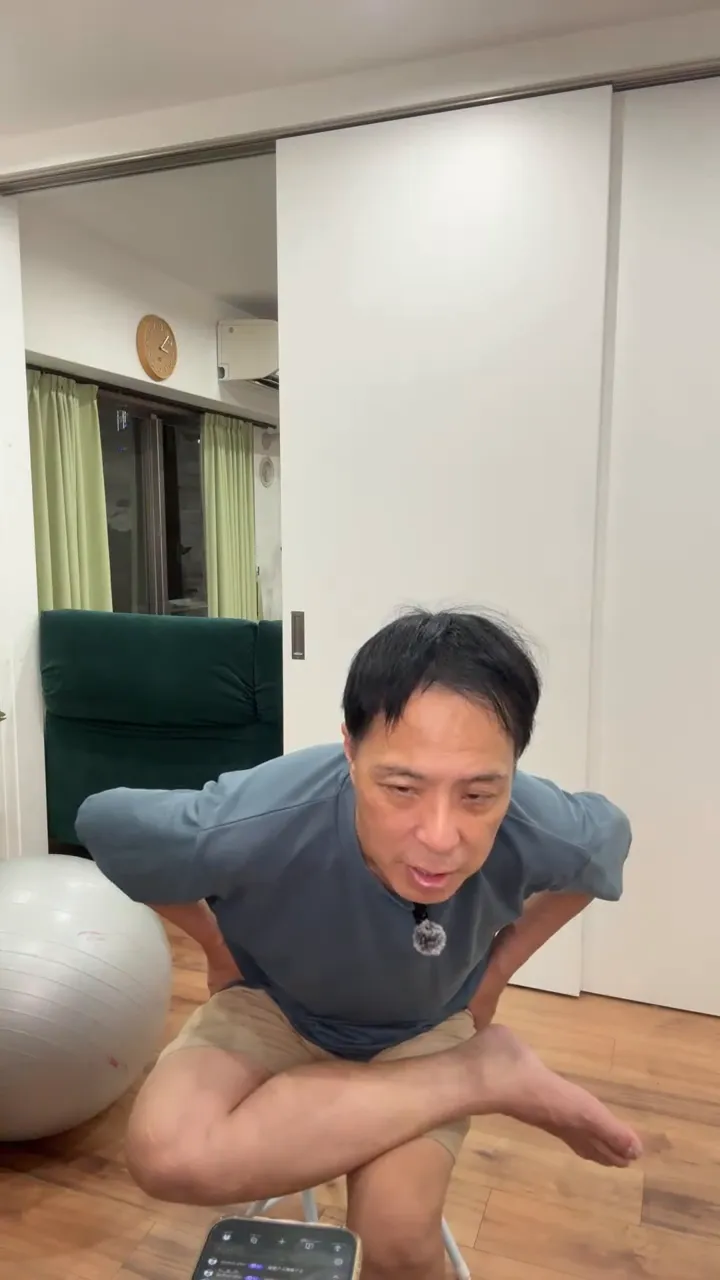 椅子に座って片脚を反対側の太ももに乗せ、両手を腰に当てて上体を前に傾けている姿勢