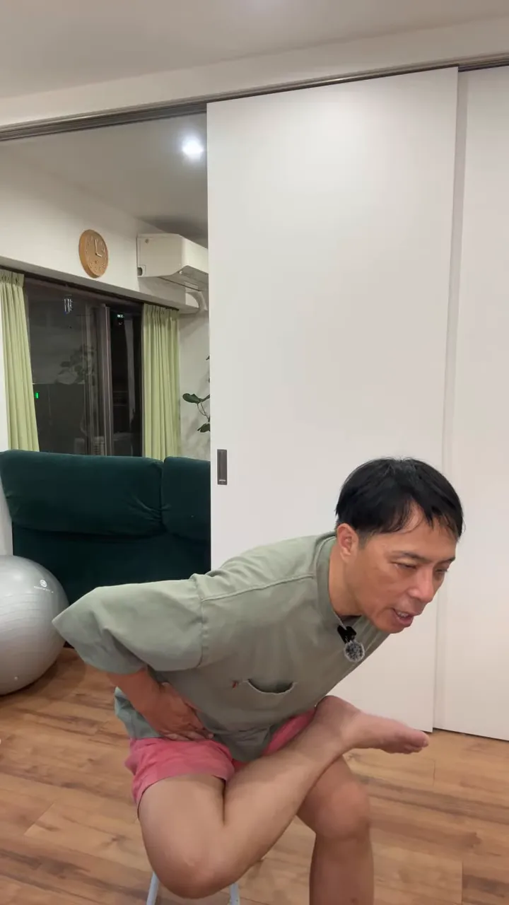 椅子に座って片足首を反対の太ももに乗せ、上体を前に傾けている姿
