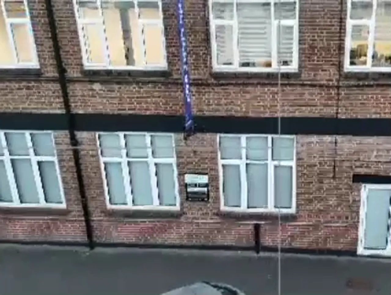 Clear drone shot of a brick building facade with aligned windows, door and street below