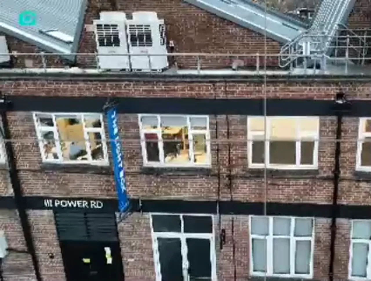 clear drone view of a brick facade with rooftop equipment, scaffolding and a blue banner