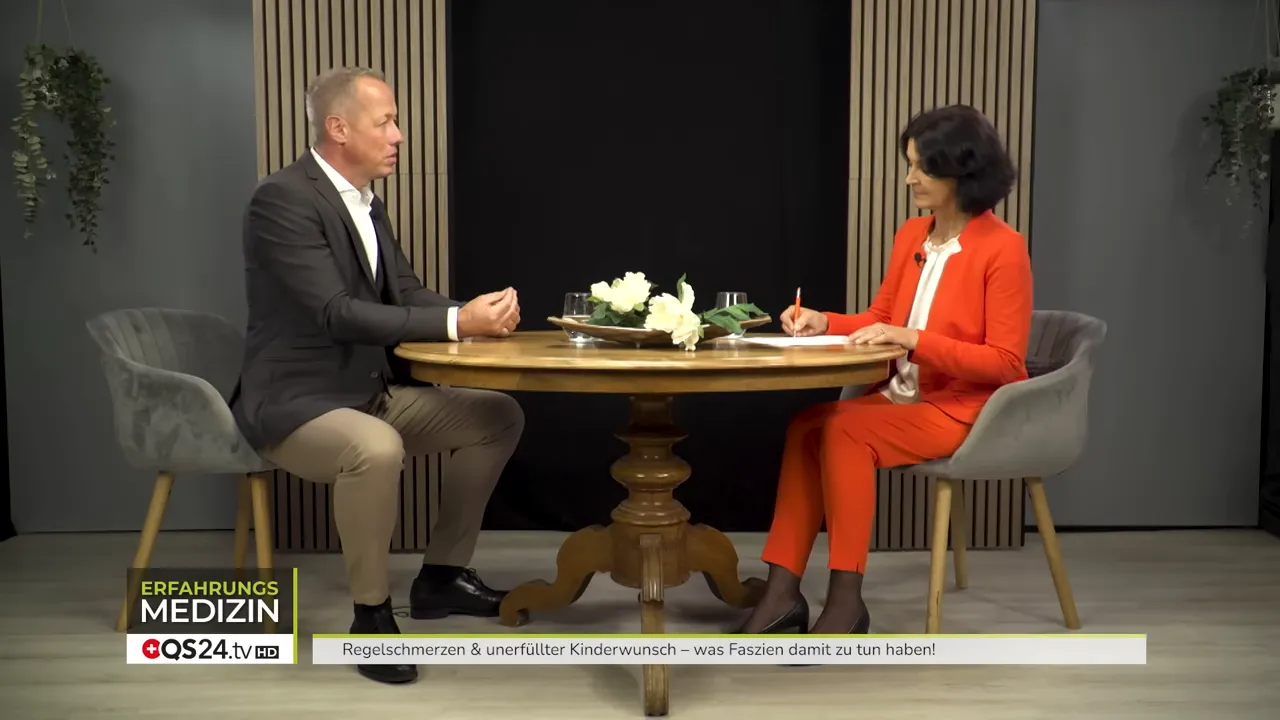 Breite Studioaufnahme von Moderatorin und Experte im Gespräch, Tischansicht