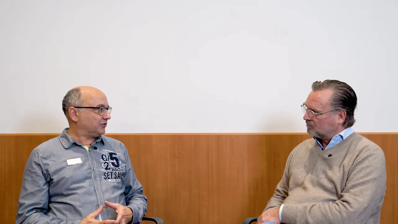 Zwei Männer im Gespräch in einer Praxis; links der Sprecher, rechts sein Gesprächspartner