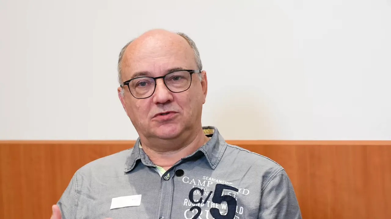 Interviewaufnahme: Mann gestikuliert mit Hand, betont einen Punkt vor hellem Hintergrund