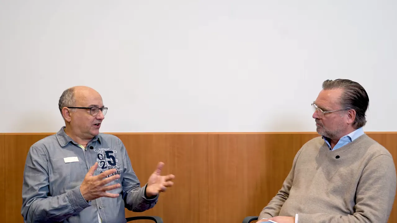 Zwei Männer im Gespräch, linker Mann gestikuliert erklärend, rechter Mann hört zu