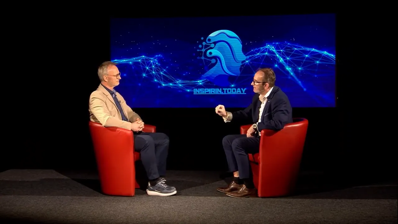 Zwei Experten im Gespräch auf der Bühne, großes blaues Display mit Logo hinter ihnen