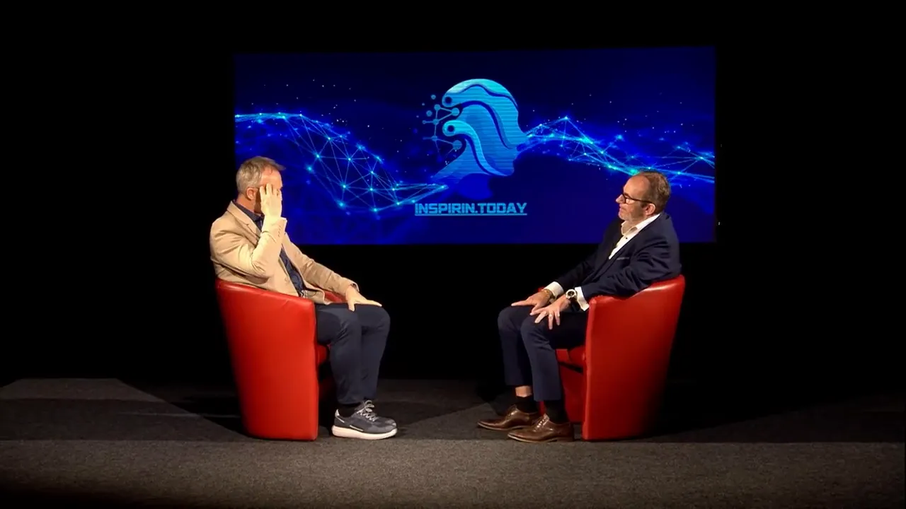 Zwei Gesprächspartner sitzen sich in roten Sesseln gegenüber, im Hintergrund großes Display mit Inspirin.Today-Logo und digitaler Grafik