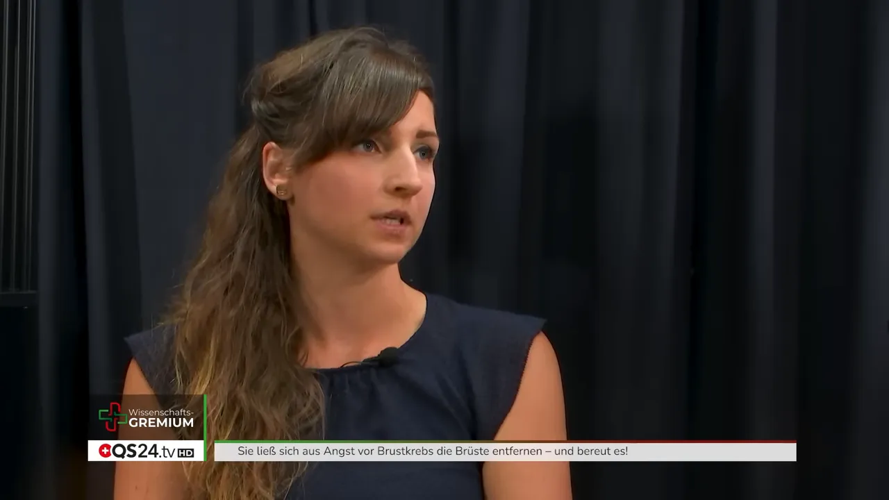 Halbkörperaufnahme einer Frau im Interview, ruhiger und nachdenklicher Ausdruck vor schwarzem Vorhang.