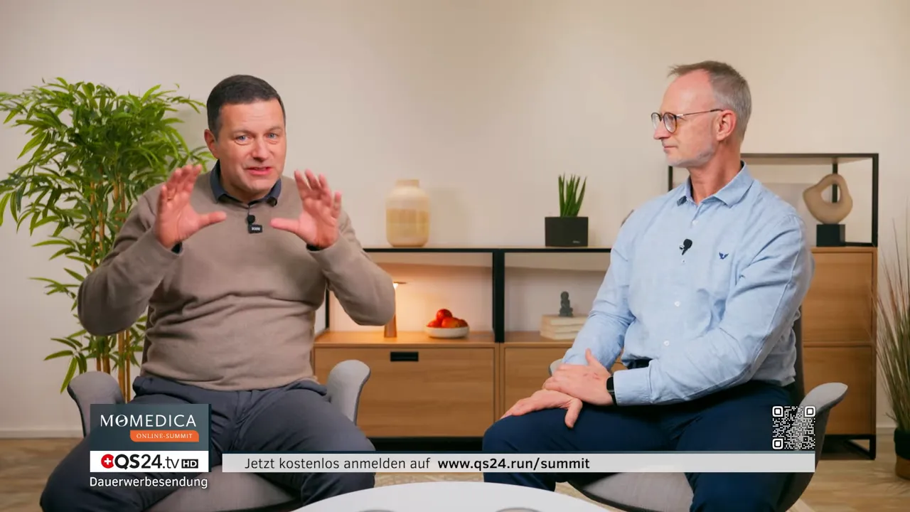 Zwei sitzende Referenten unterhalten sich in einem Studio-Setting; einer gestikuliert, Regal mit Dekor im Hintergrund, Anmeldeeinblendung unten.