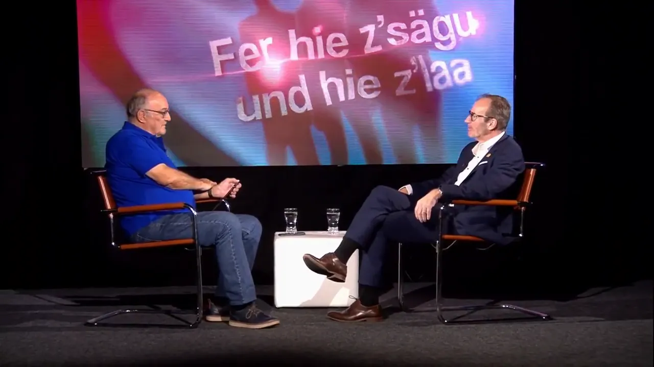 Zwei Gesprächspartner auf einer Bühne vor einer großen Videowand mit Projektion, Studioatmosphäre