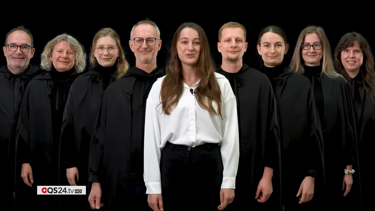 Klares Gruppenporträt des QS24 TV Ensembles, Frontfrau in weißem Hemd, Team in schwarzen Roben auf dunklem Hintergrund