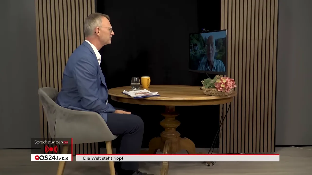 Weitwinkelaufnahme: Moderator im Studio am Tisch, zugeschalteter Gast auf Monitor, Untertitel 