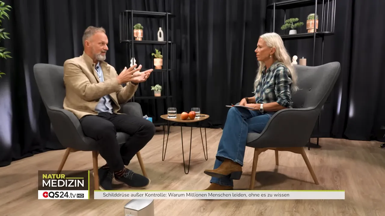 Wie die Schilddrüse Ihr Leben bestimmt - Interview mit Dr. Markus Stark, Ernährungsexperte und Dozent für Psycho‑Neuro‑Immunologie 1 Weitaufnahme des Interviews mit Expert:in und Moderatorin, Studioeinrichtung und Tisch mit Gläsern sichtbar.