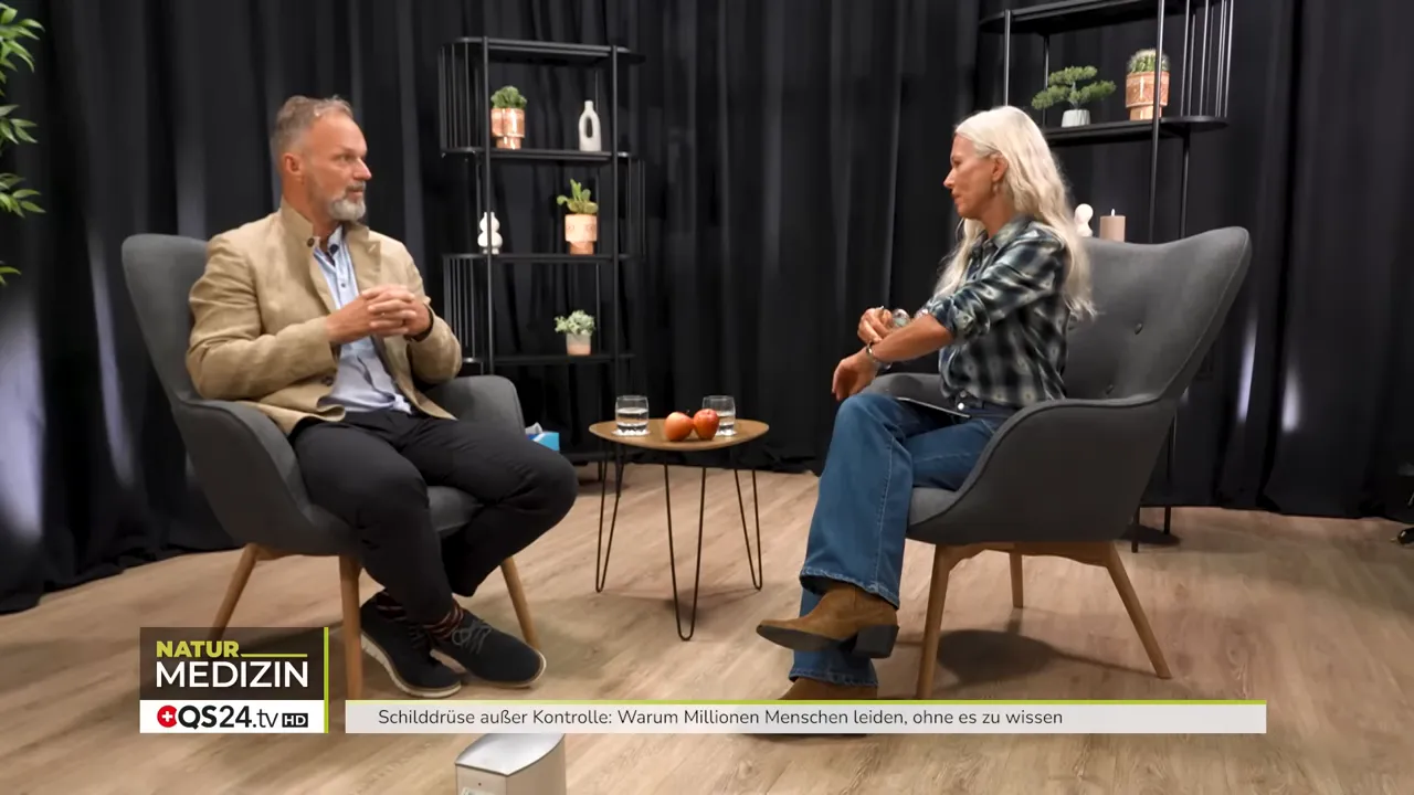 Wie die Schilddrüse Ihr Leben bestimmt - Interview mit Dr. Markus Stark, Ernährungsexperte und Dozent für Psycho‑Neuro‑Immunologie 6 Weitaufnahme des Interviews: Dr. Markus Stark und die Moderatorin sitzen einander gegenüber; kleiner Tisch mit Äpfeln und Wassergläsern sichtbar