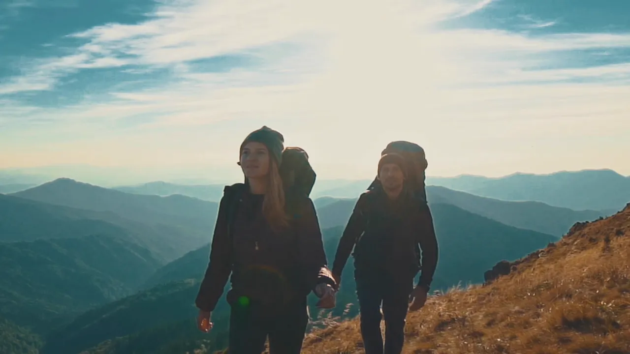 Zwei Wanderer mit Rucksäcken auf einem Berggrat bei Sonnenaufgang