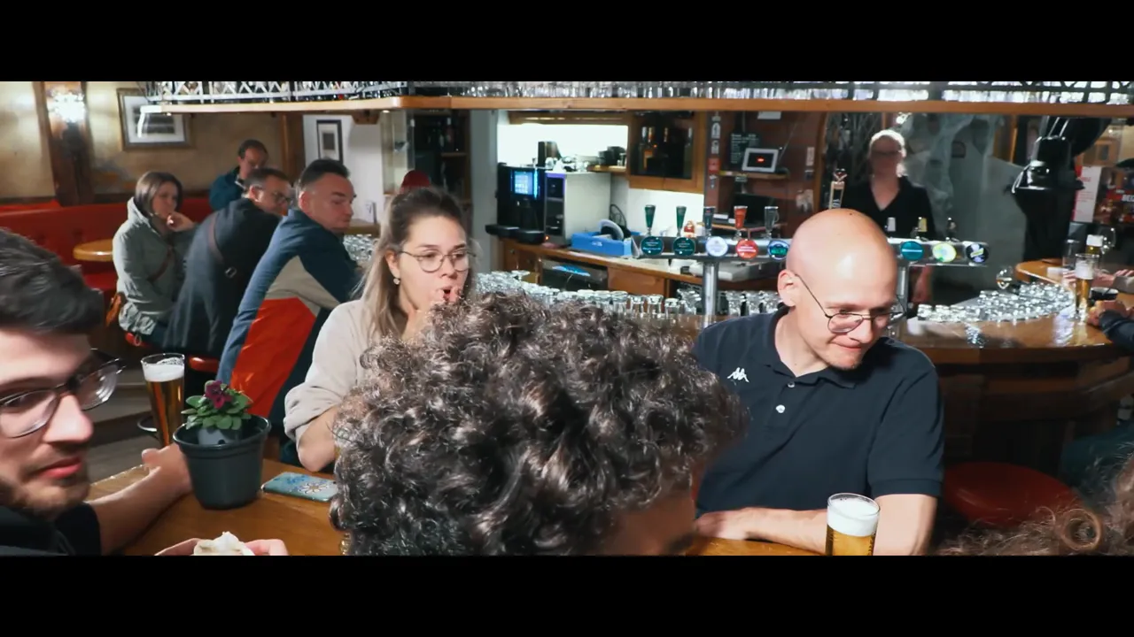 Gäste sitzen an der Bar im Bäji‑Pub mit Biergläsern und Zapfanlage im Hintergrund
