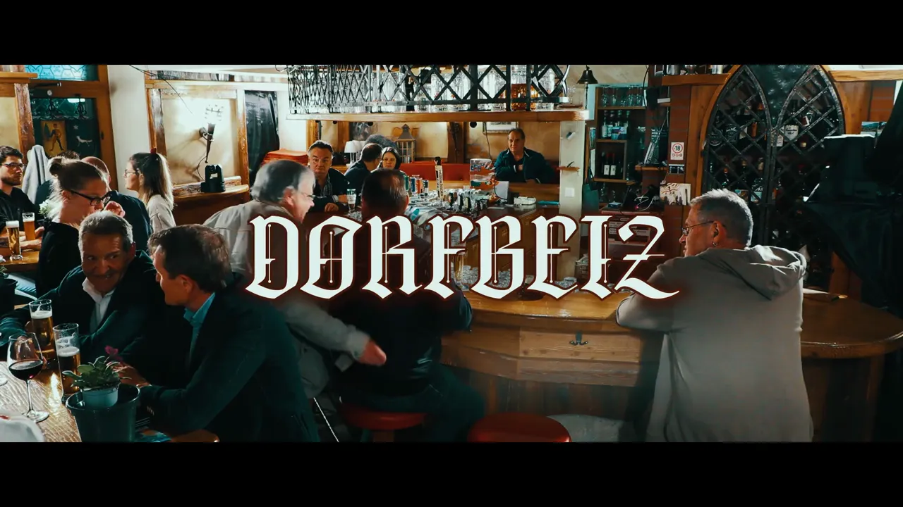 Weitwinkelaufnahme einer belebten Dorfbeiz mit dem Schriftzug 'Dorfbeiz' über der Bar