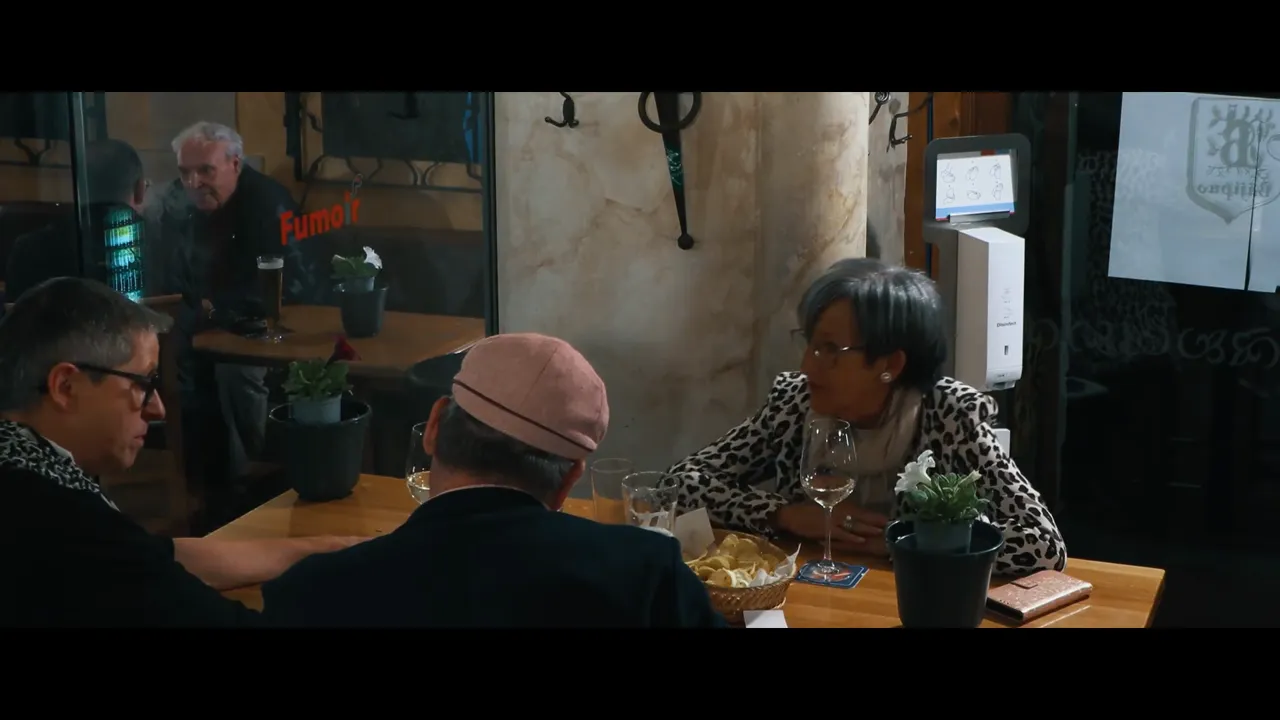 Gästetisch im Bäji-Pub mit drei Personen, Weinglas, Bierglas, Snacks und Spiegelung mit Schrift 'Fumoir'.