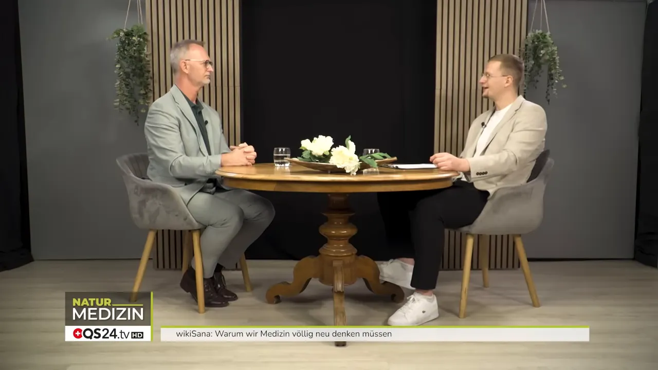 Warum wir Medizin völlig neu denken müssen - Das Interview mit Alexander Glogg, Gründer von wikiSana und QS24, Brückenbauer zwischen Schulmedizin und Ganzheitsmedizin 4 Zwei Personen sitzen einander gegenüber an einem runden Tisch im Studio, Studiodekoration und Einblendung 'Natur Medizin' unten links
