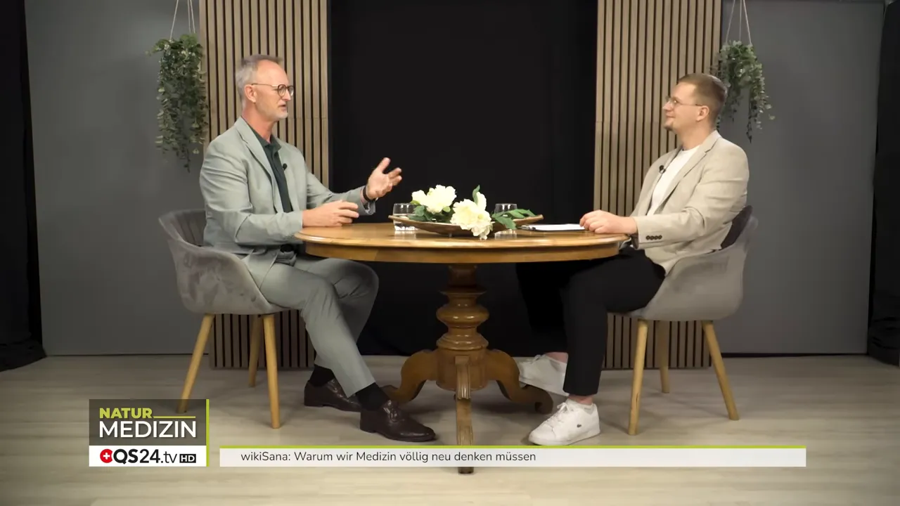 Warum wir Medizin völlig neu denken müssen - Das Interview mit Alexander Glogg, Gründer von wikiSana und QS24, Brückenbauer zwischen Schulmedizin und Ganzheitsmedizin 6 Weitaufnahme des runden Interviewtisches mit Alexander Glogg und Moderator, beide im Gespräch, Studioeinrichtung sichtbar