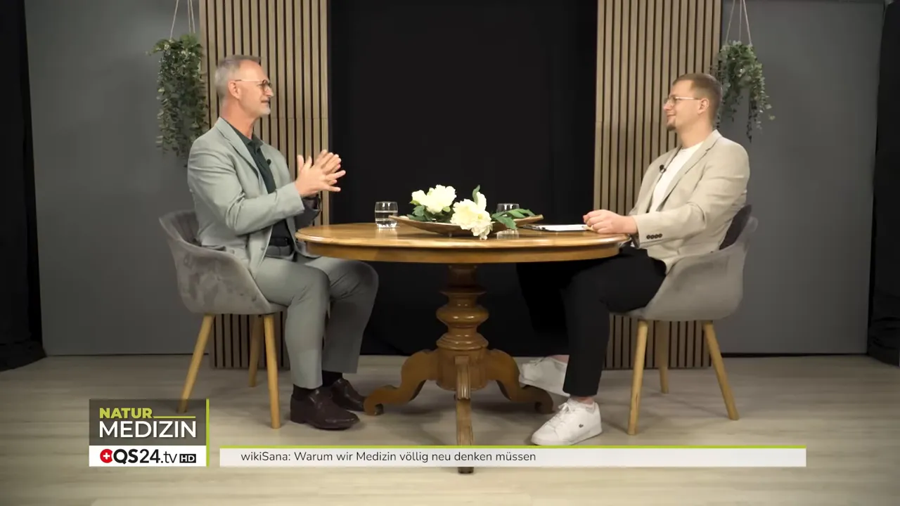 Warum wir Medizin völlig neu denken müssen - Das Interview mit Alexander Glogg, Gründer von wikiSana und QS24, Brückenbauer zwischen Schulmedizin und Ganzheitsmedizin 2 Weitaufnahme des Studiotisches mit Alexander Glogg und dem Moderator im Gespräch