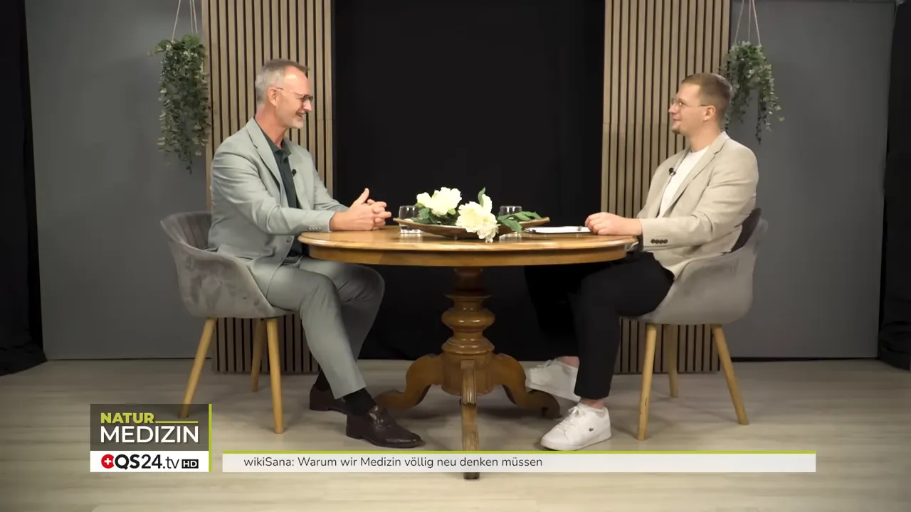 Warum wir Medizin völlig neu denken müssen - Das Interview mit Alexander Glogg, Gründer von wikiSana und QS24, Brückenbauer zwischen Schulmedizin und Ganzheitsmedizin 7 Zwei Gesprächsteilnehmer sitzen an einem runden Tisch im Studio, Weitaufnahme, im Gespräch