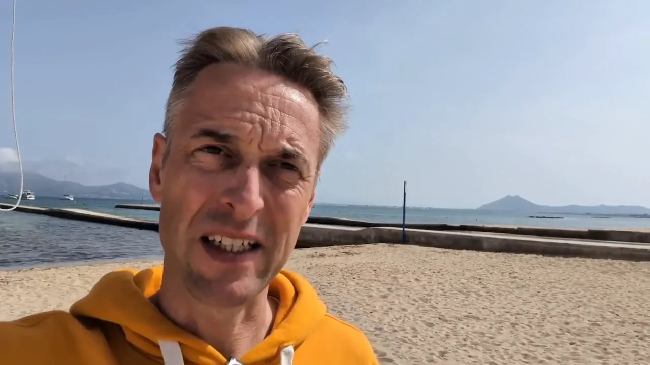 Gut komponierte Aufnahme: Mann im gelben Kapuzenpullover am Strand mit Küste im Hintergrund