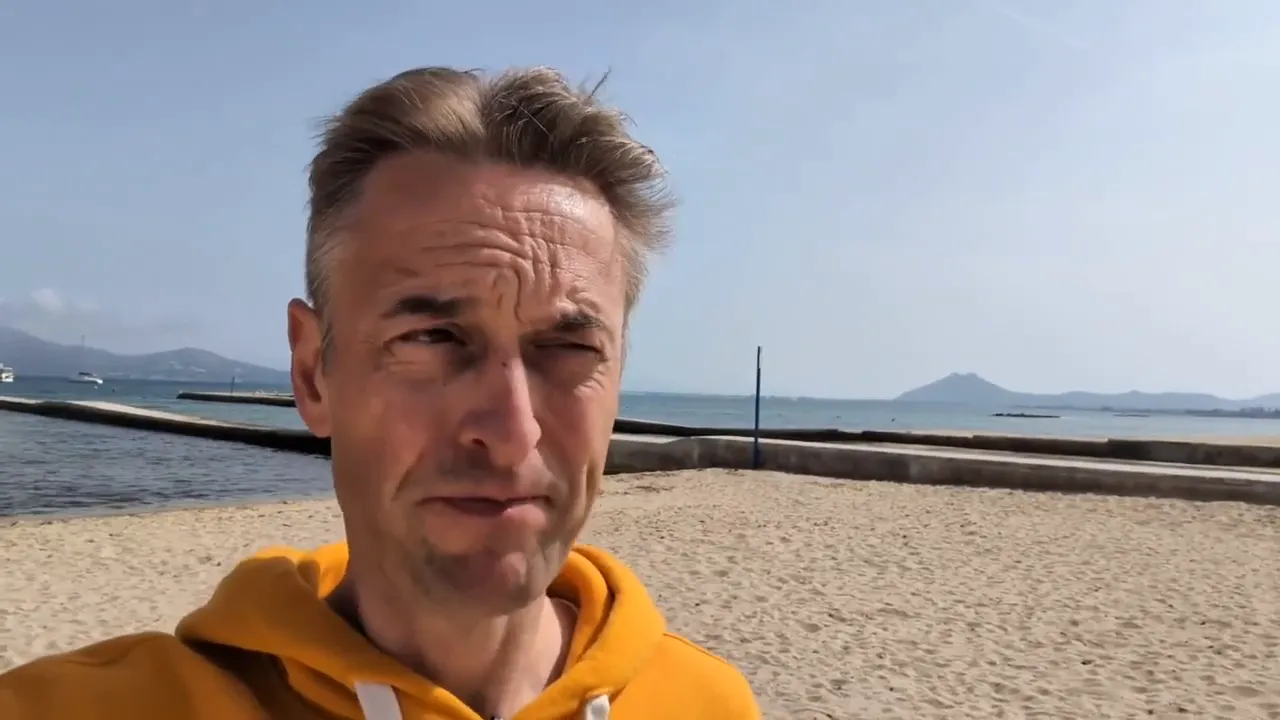 Berater im gelben Hoodie am Strand mit klar sichtbarem Meer und Ufer; Momentaufnahme aus einem Video