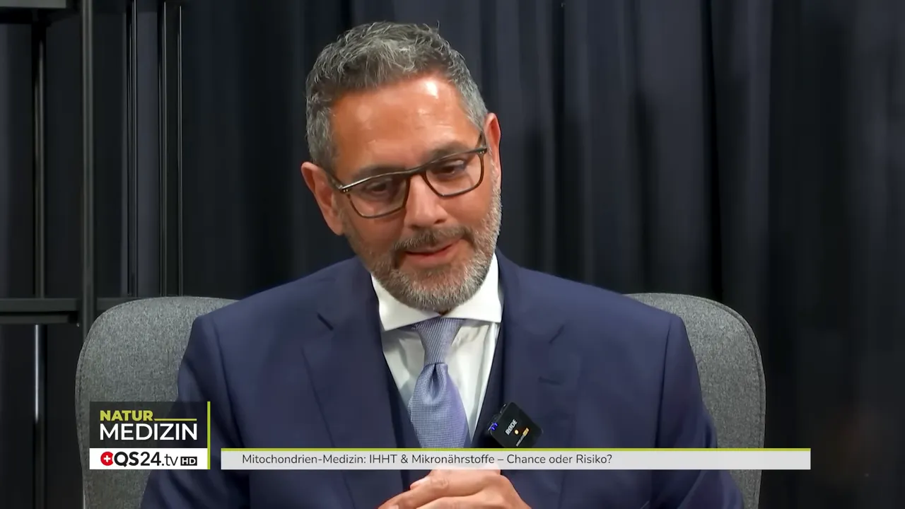 Dr. Popat blickt nach unten, wirkt nachdenklich während er über Praxisbeispiele in der Mitochondrien‑Medizin spricht.