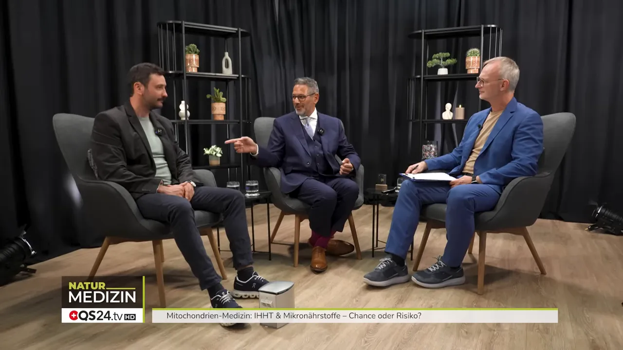 Drei Personen im Studiogespräch; der mittlere Experte zeigt mit ausgestrecktem Arm und gestikuliert dabei.