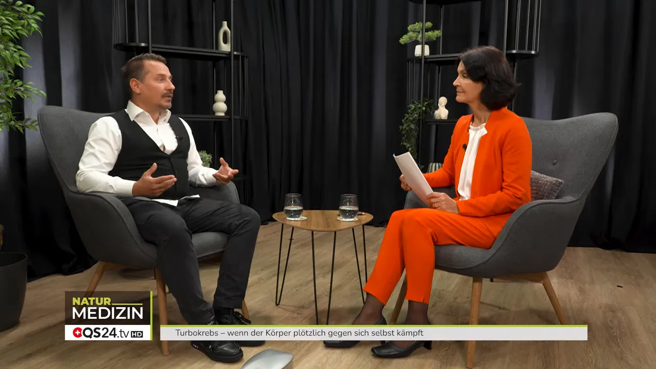 Weitwinkelaufnahme eines Studio-Interviews: der Gast erklärt gestikulierend, Moderatorin hört zu