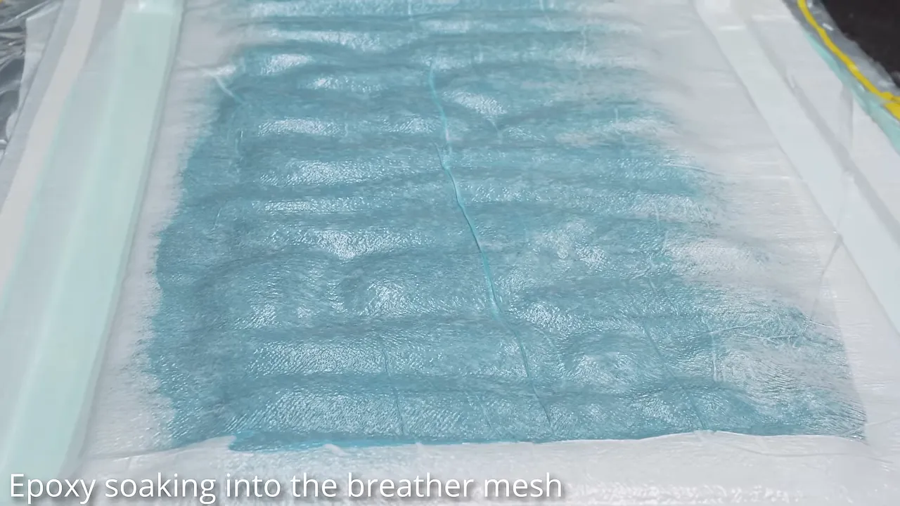 Large rectangular denim layup compressed beneath clear vacuum film with pale material around its perimeter