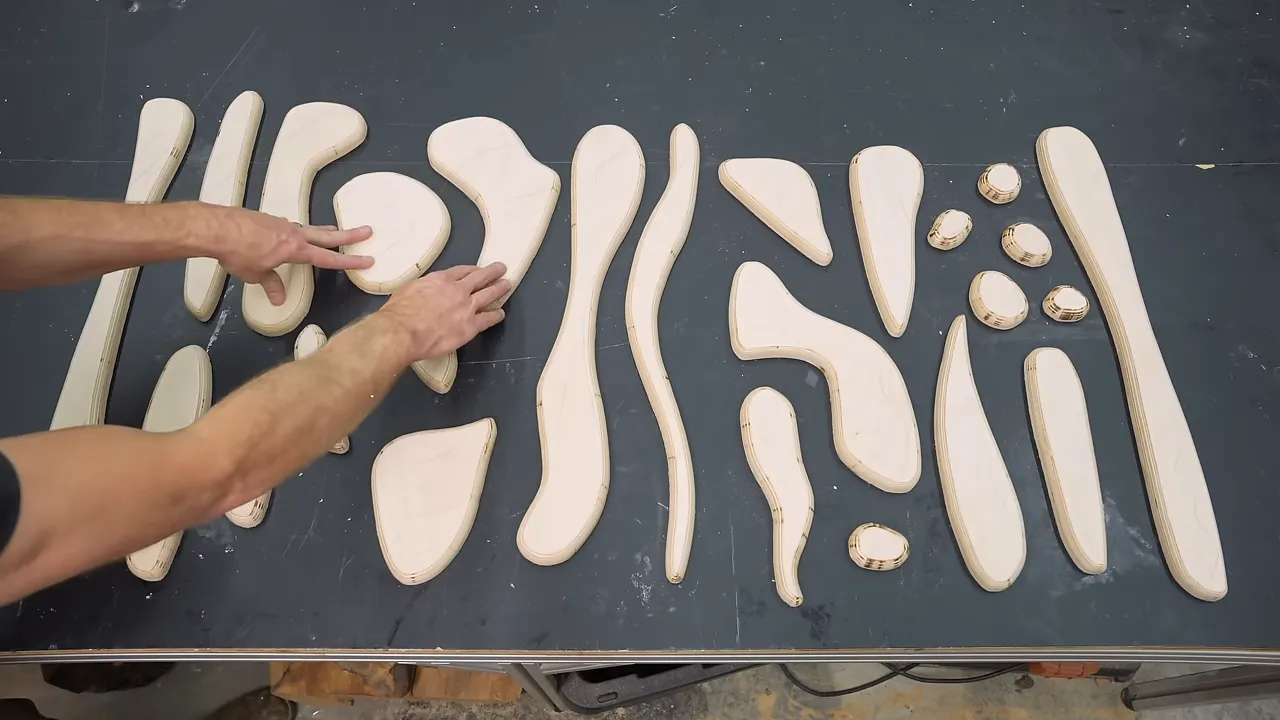 Overhead layout of curved plywood strips and small circles on a dark work surface