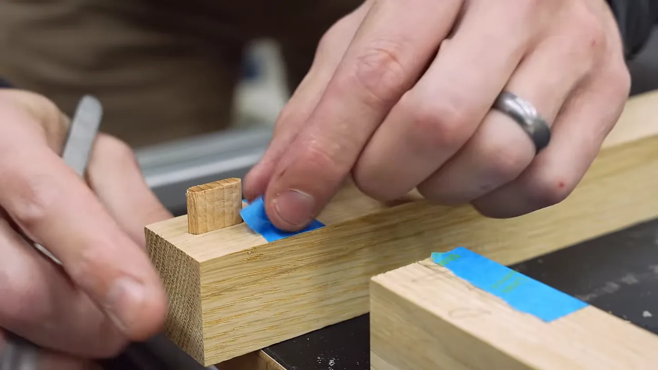 Blue painter's tape masking the inside corner of a white oak frame joint