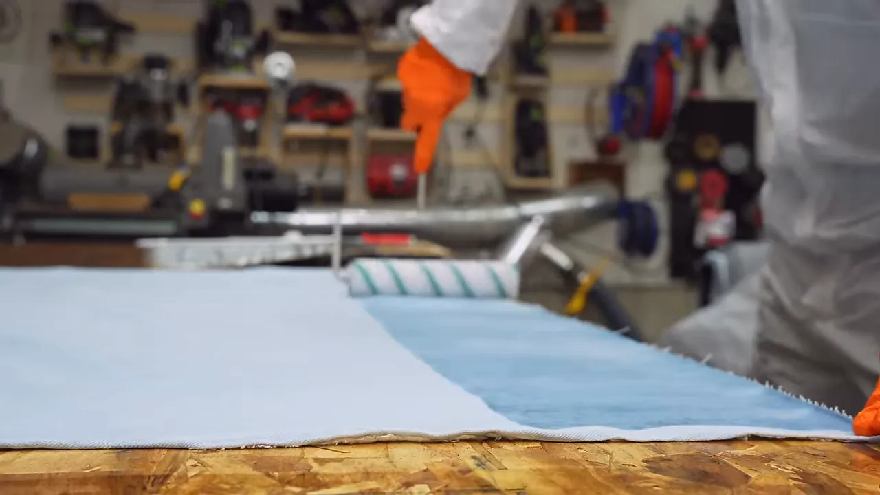Roller spreading epoxy across a light blue sheet of denim