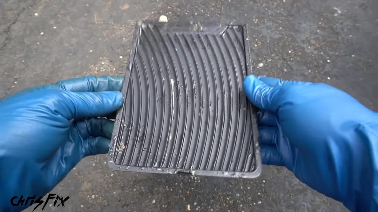 Gloved hands holding a cleaned ribbed rubber console insert above removed debris