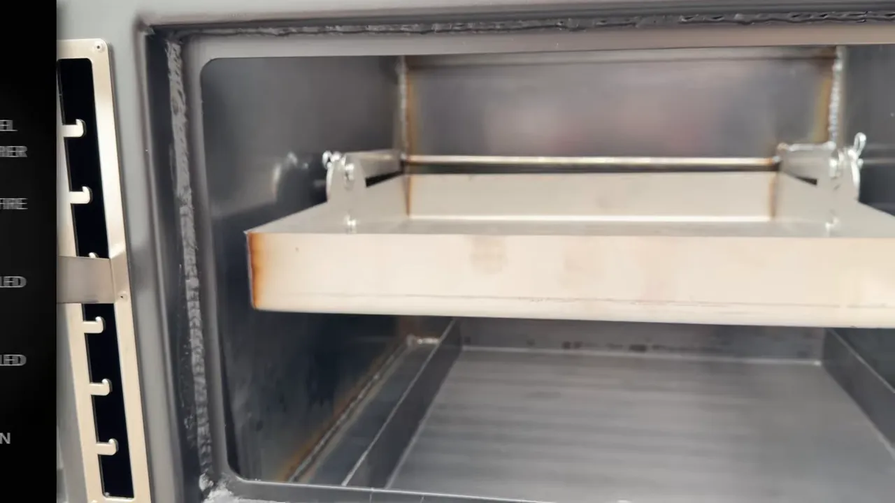 Open front firebox showing a slotted charcoal grate, adjustment rails, and an ash pan below