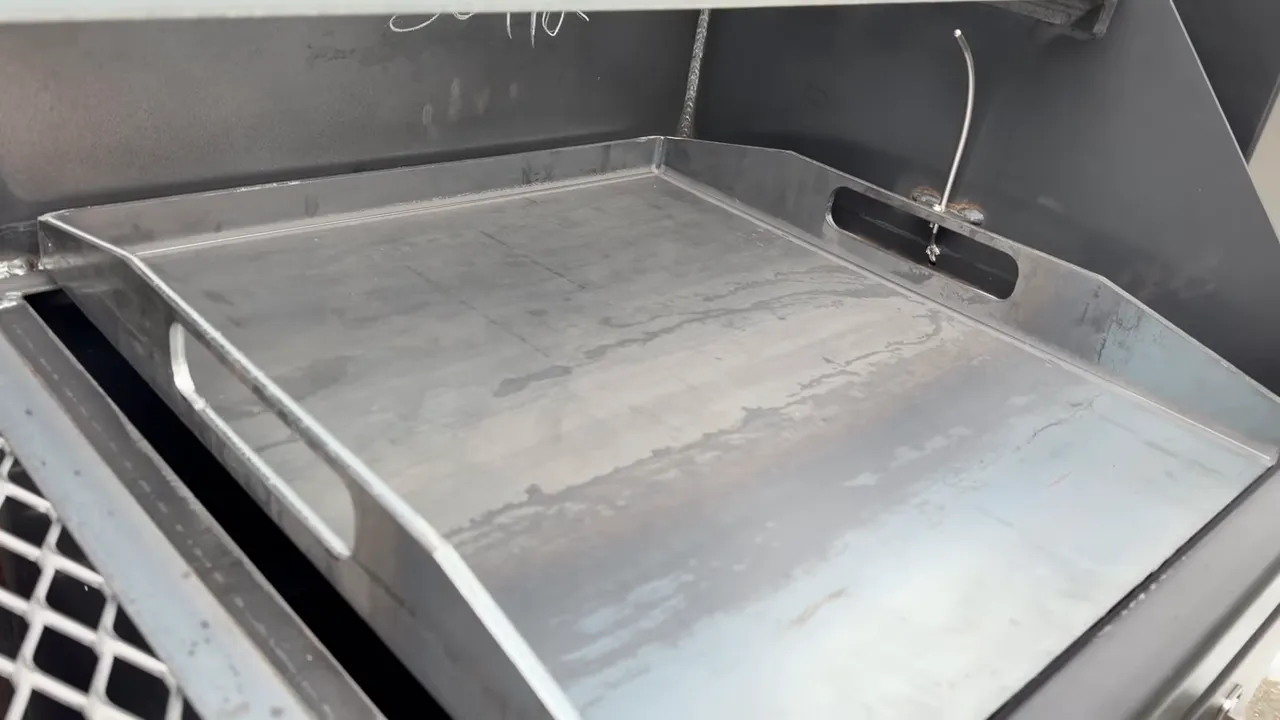 Rectangular steel plancha positioned beneath the upper cooking rack