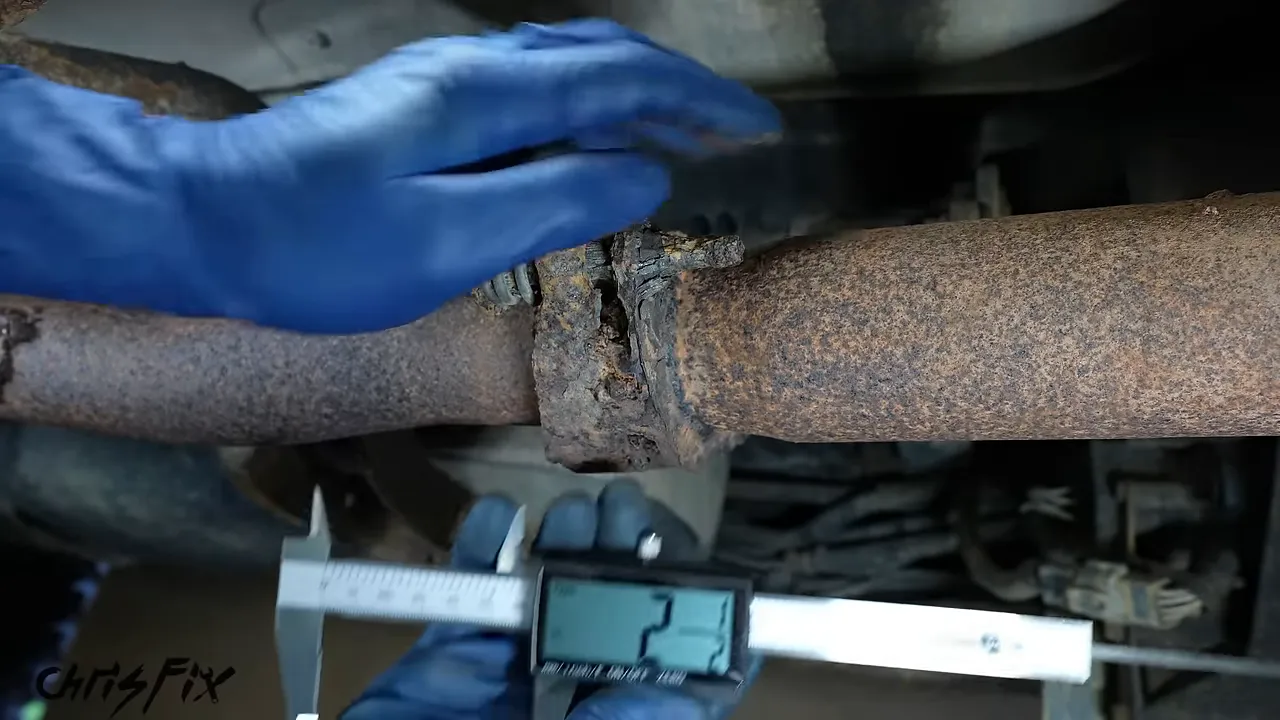 Digital caliper measuring the larger exhaust pipe beside a rusty flange