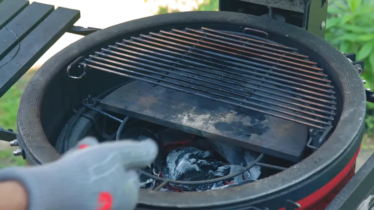 Open kamado with a rear cooking grate above one heat deflector and exposed charcoal at the front