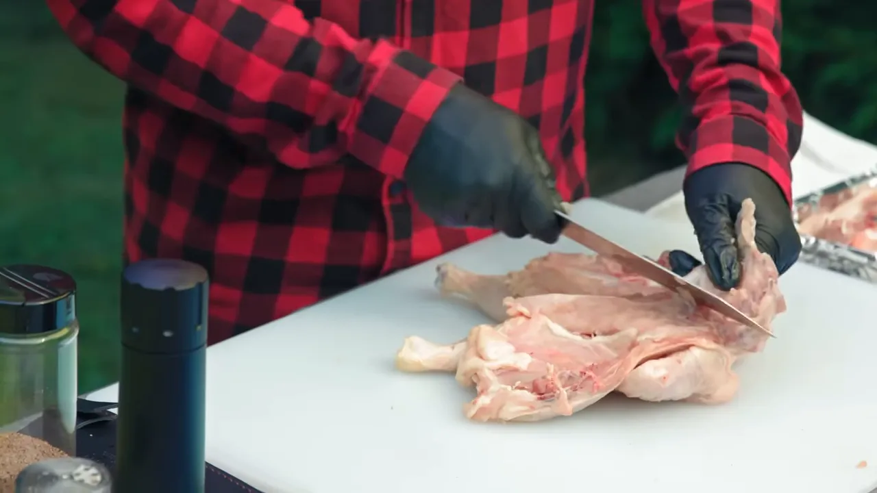Gloved hands lifting rib bones while cutting them away from the opened chicken
